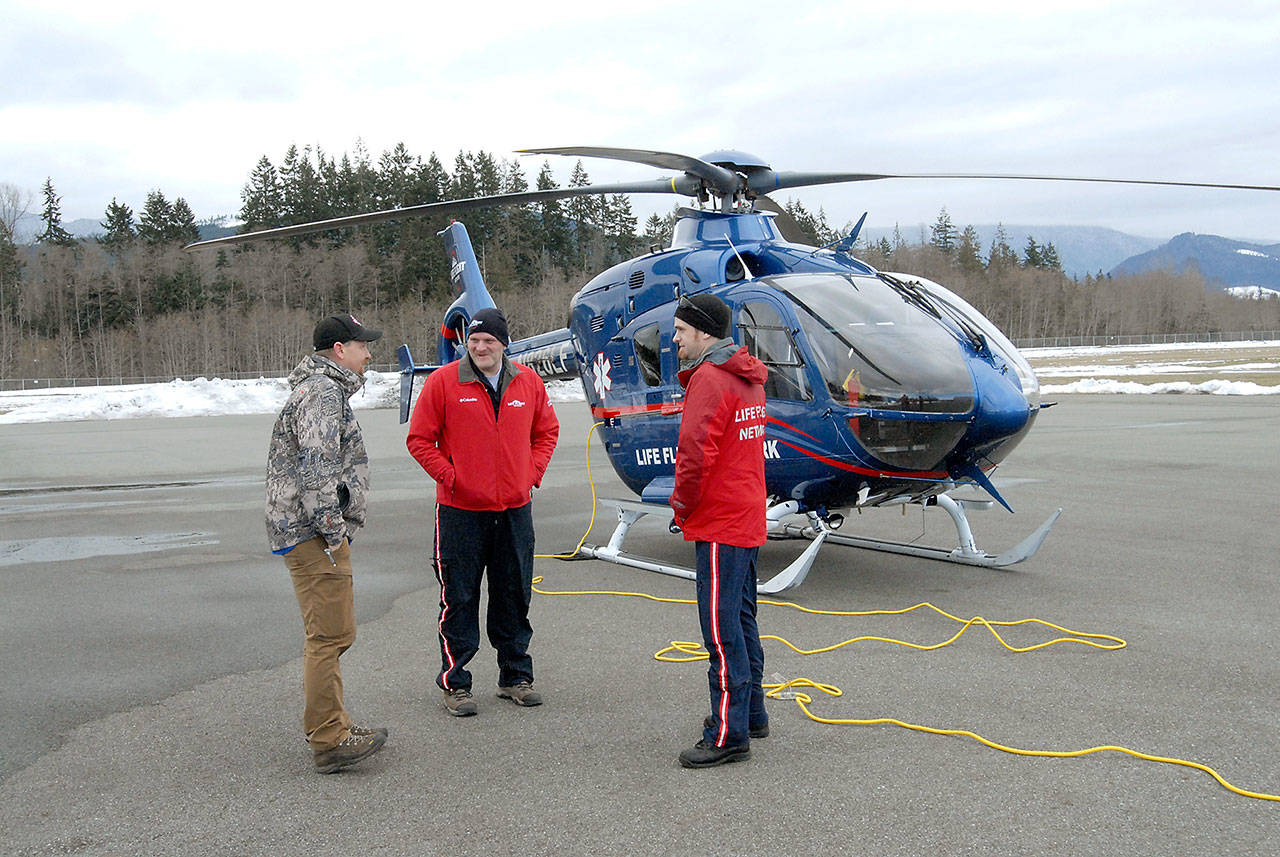 Port Angeles firefighter Mark Karjalainen, left, speaks with Life Flight Network personnel David Salisbury, center, and Garth Hope-Melnick next to an on-call EC-135 medical transport helicopter at William R. Fairchild International Airport in Port Angeles. (Keith Thorpe/Peninsula Daily News)