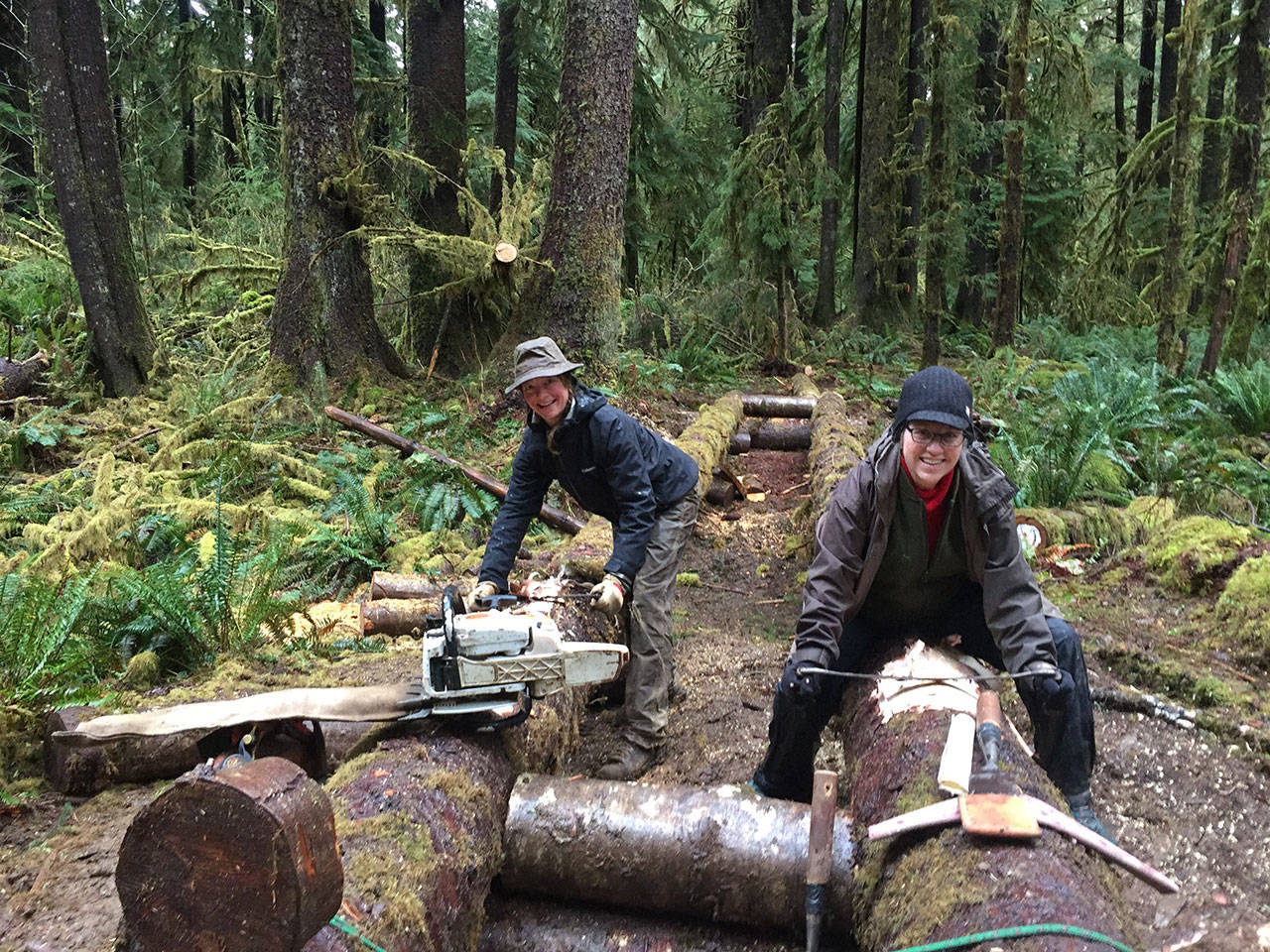 Sherry Baysinger, right, and Heidi Brill — members of the Mount Olympus Chapter of Back Country Horsemen — peel bark off the stringers for an elevated puncheon as part of an ongoing project putting a new bypass trail on the Bogachiel River trail. (Larry Baysinger)