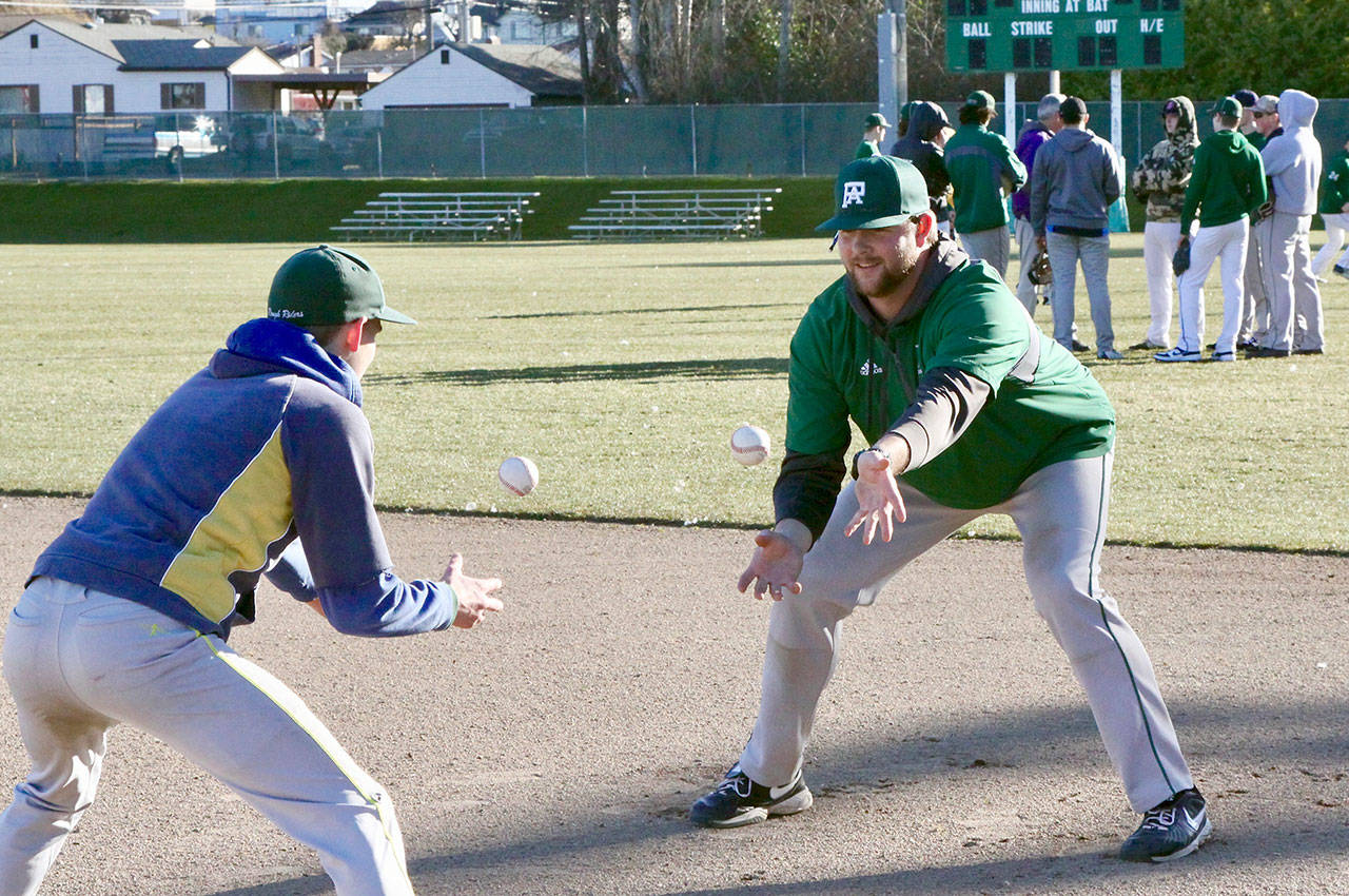 Dave Logan/for Peninsula Daily News Port Angeles baseball coach Karl Myers, right, and infielder Daniel Basden practice the two-ball juggle during the team’s first outdoors practice of the season at Civic Field on Tuesday.
