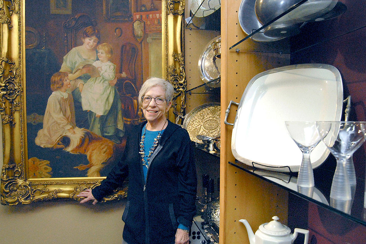 Necessities & Temptations owner Edna Petersen, shown next to a painting that has served as a central theme to her business, is closing up shop and liquidating most of her merchandise. (Keith Thorpe/Peninsula Daily News)