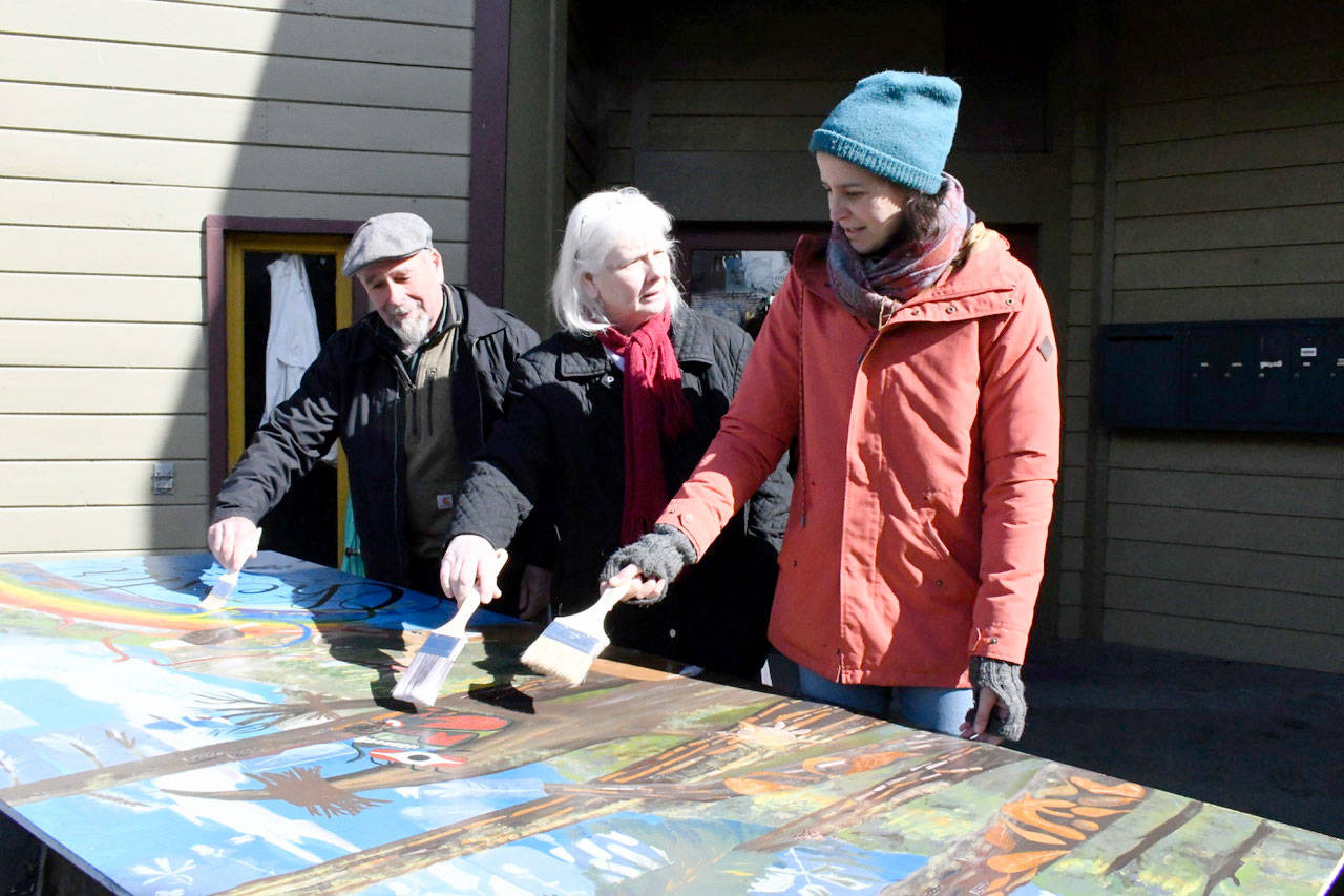 Malcolm Dorn, Adrianna Santiago and Suzanne Jones apply a final coat of clear latex over part of a community mural that will be installed Saturday at Dorn’s property known locally as Chester Square. (Jeannie McMacken/Peninsula Daily News)