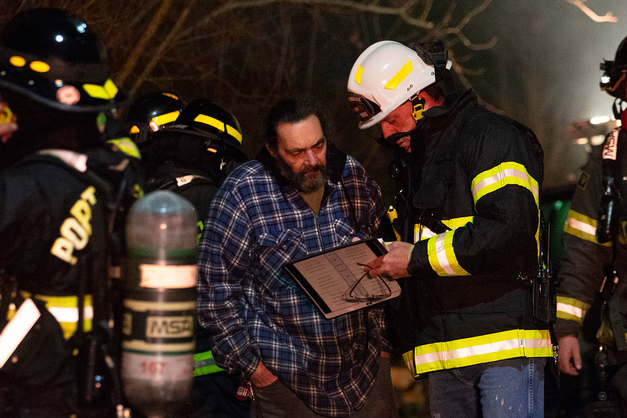 Port Angeles Fire Department Fire Marshal Michael Sanders talks with Harold Bushman Wednesday night as firefighters extinguish the fire at his Port Angeles home. (Jesse Major/Peninsula Daily News)
