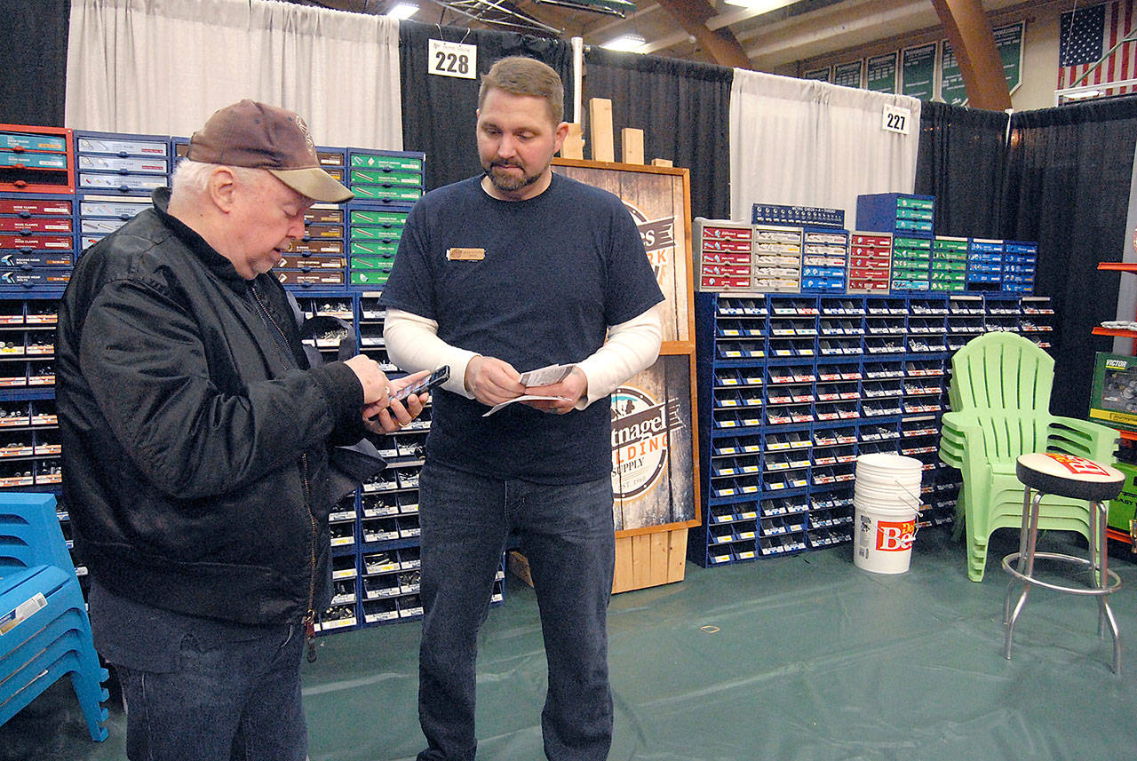 Jim Doherty of Port Angeles, left, consults his cellphone while talking about home improvement with Rick North of Angeles Millwork Lumber Co., and Hartnagel Building Supply at a vendor booth on Saturday. (Keith Thorpe/Peninsula Daily News)