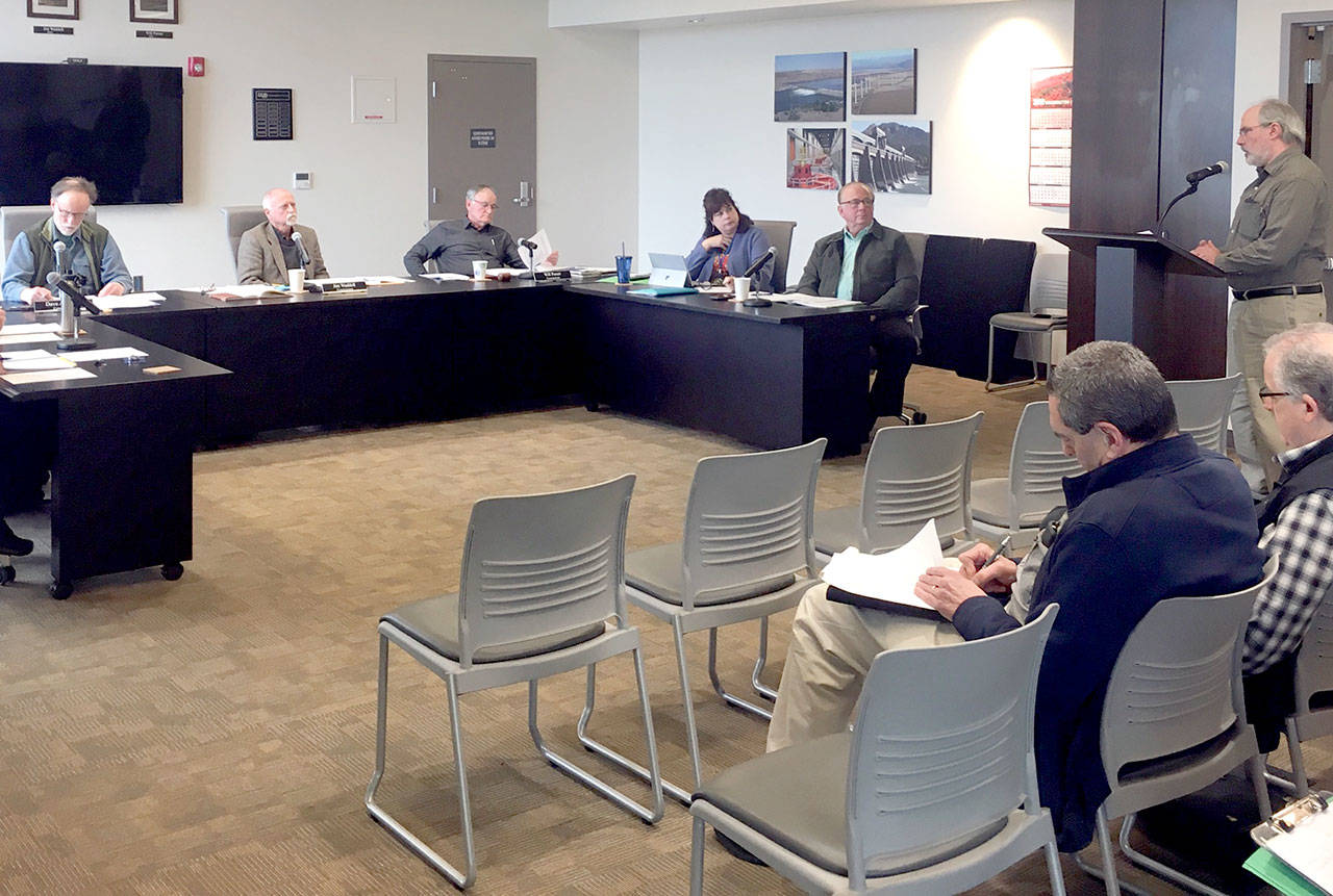 Clallam County Public Utility District Commissioners David Anderson, left, Jim Waddell and Will Purser listen as Assistant Manager John Purvis speaks from the podium. (Rob Ollikainen/Peninsula Daily News)