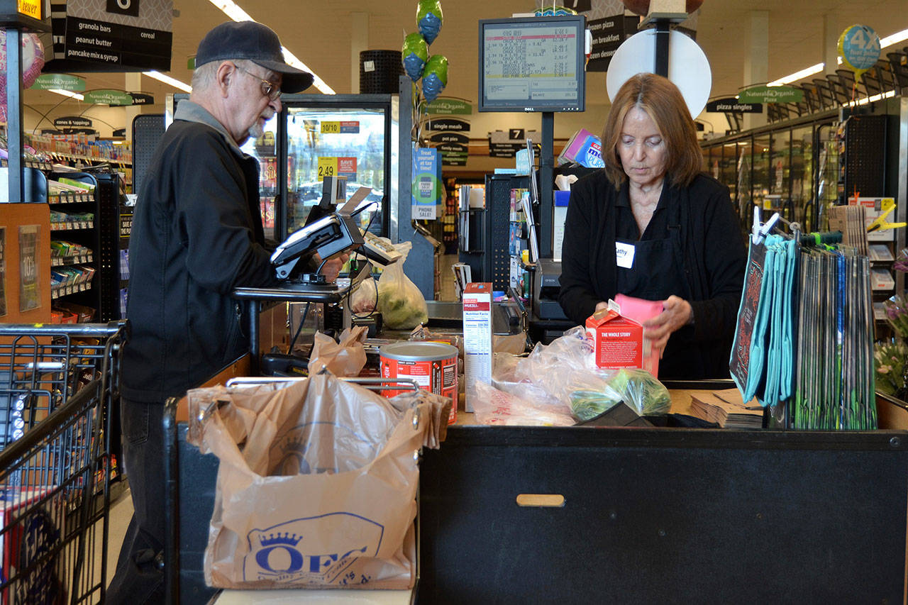 Kathy Johnson, a checker at Sequim QFC, helps Jack Guinn purchase his groceries on March 18. Starting Monday, the store will no longer offer plastic bags at checkout stands to customers. (Matthew Nash/Olympic Peninsula News Group)