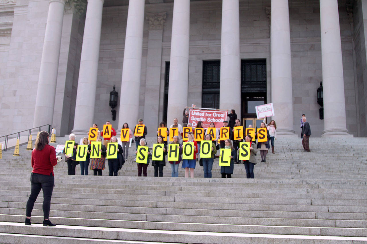 Seattle Public School’s librarians hold up signs on the Capitol building steps in protest of funding cuts that have resulted in cuts to libraries. Kate Eads, who organized the event, can be seen holding a megaphone addressing the group. (Emma Epperly/WNPA Olympia News Bureau)