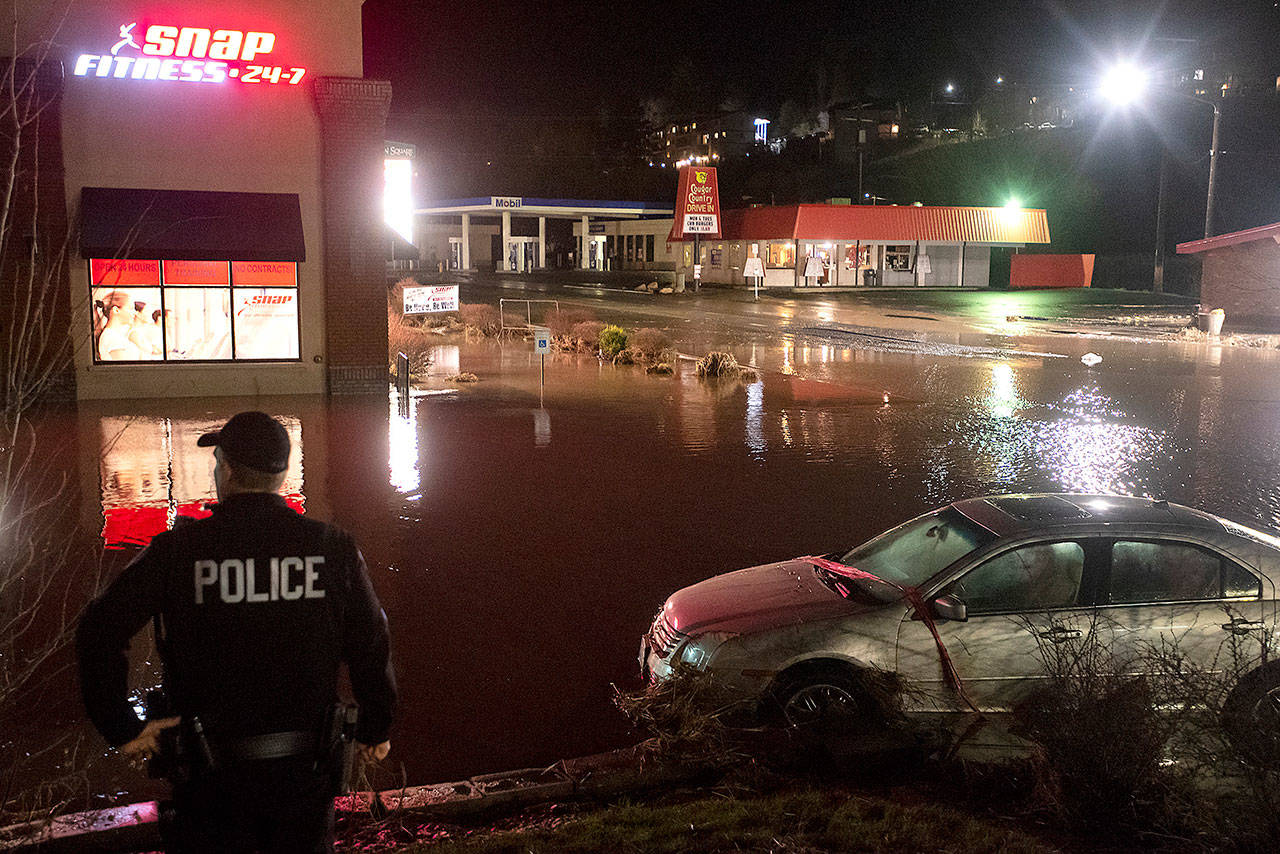 An officer from the Pullman Police Department assesses the water damage to a car in a parking lot along Grand Avenue in Pullman on Tuesday. (Pete Caster/Lewiston Tribune via AP)