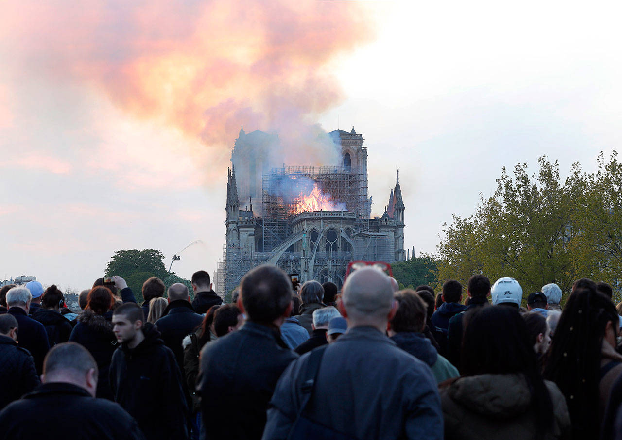 People watch as flames and smoke rise from Notre Dame Cathedral as it burns in Paris today. (Thibault Camus/The Associated Press)