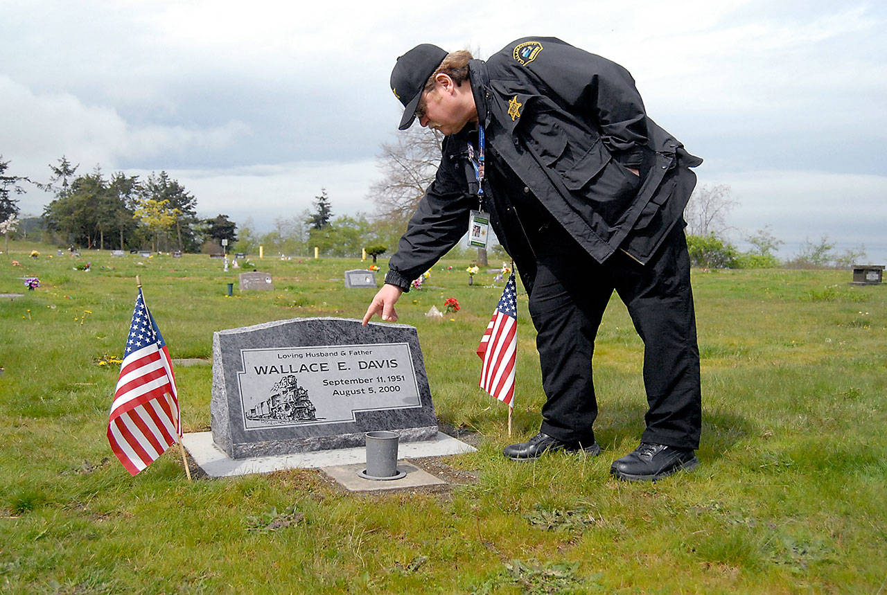 Randy Pieper, forensic evidence manager for the Clallam County Sheriff’s Office, points to features on a headstone at the grave of the late Deputy Wally Davis on Thursday at Ocean View Cemetery in Port Angeles. (Keith Thorpe/Peninsula Daily News)