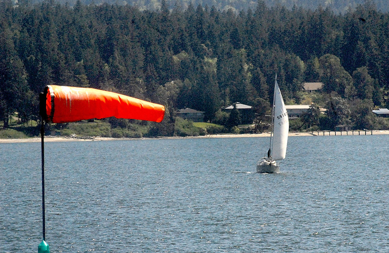 A windsock at John Wayne Marina near Sequim indicates the wind direction as a sailboat plies the waters of Sequim Bay on Tuesday. (Keith Thorpe/Peninsula Daily News)