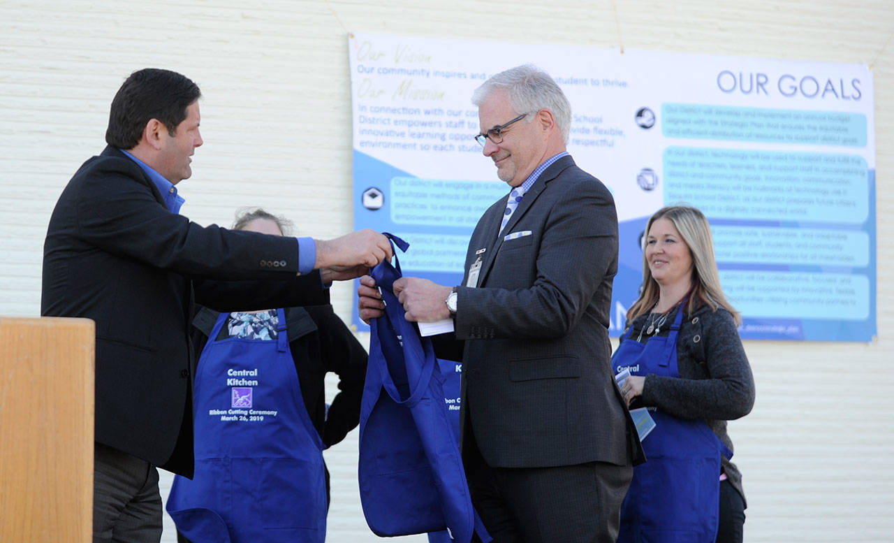 Sequim School District Superintendent Gary Neal, right, receives an honorary apron from Bernie O’Donnell, vice president/northwest area manager for Vanir, as school representatives and officials celebrate the opening of the Sequim School District’s new central kitchen March 26. (Michael Dashiell/Olympic Peninsula News Group)