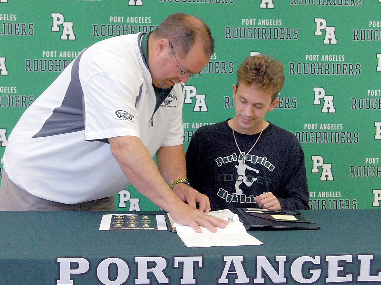 Keith Thorpe/Peinsula Daily News Port Amgeles High School athletic director Dwayne Johnson, left, goes over paperwork on Wednesday with Andrew St. George as St. George signs a letter of intent to attend Peninsula College.