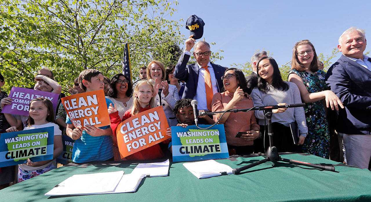 Gov. Jay Inslee, center, pulls off his “100%” cap, standing for a goal of 100 percent clean energy, after posing for a photo with supporters after signing climate protection legislation Tuesday in Seattle. (Elaine Thompson/The Associated Press)