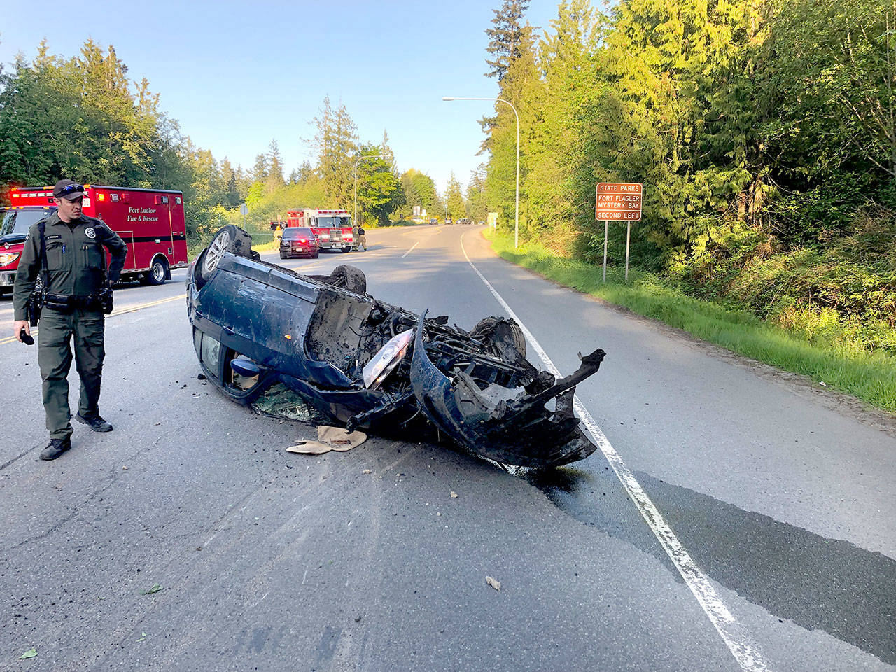 Jefferson County Sheriff’s Deputy Adam Newman surveys the damage to the blue BMW driven by a California man who was ejected from the vehicle Wednesday night on state Highway 116 near Oak Bay Road. The man was airlifted to Harborview Medical Center in Seattle. (Jefferson County Sheriff’s Office)