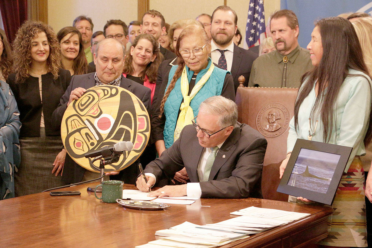 Gov. Jay Inslee, surrounded by lawmakers, tribal members and others, signs the first of several bills designed to help the Pacific Northwest’s endangered orcas on Wednesday in Olympia. goods. (Rachel La Corte/The Associated Press)