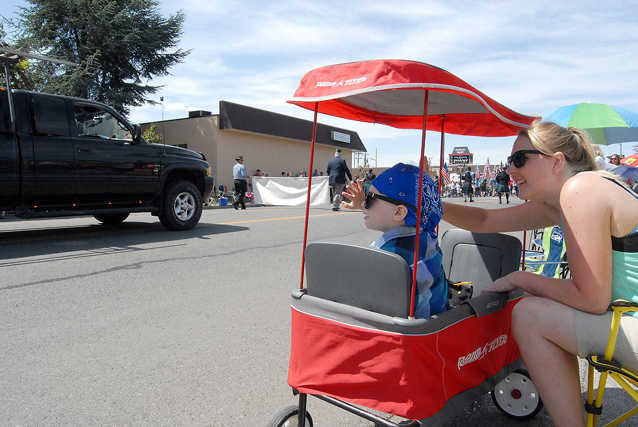 Carter Tinkham, 3, and his mother, Vanessa Tinkham, both of Sequim, wave from the curb during Saturday’s Grand Parade. (Keith Thorpe/Peninsula Daily News)