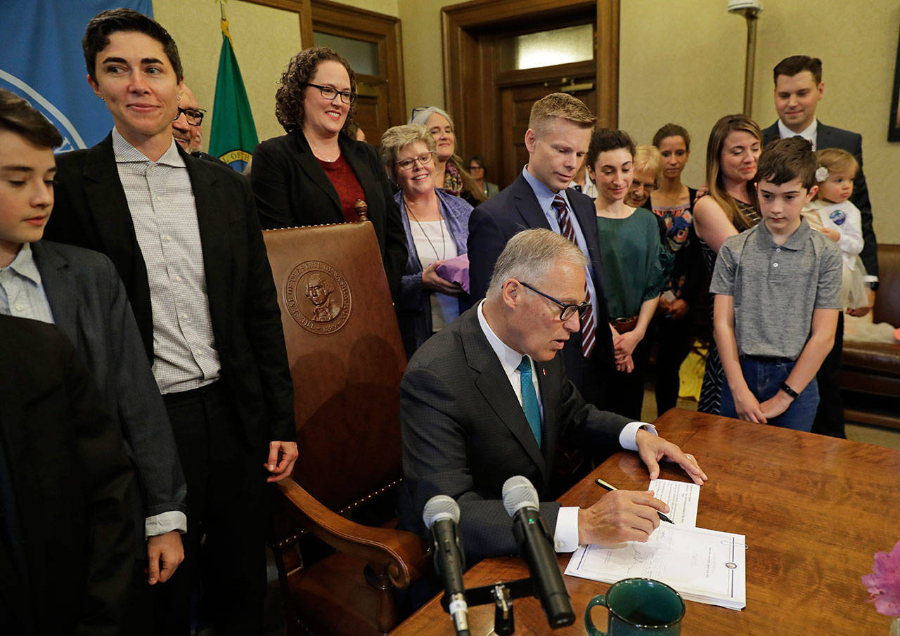 Katrina Spade, upper left, the founder and CEO of Recompose, a company that hopes to use composting as an alternative to burying or cremating human remains, looks on Tuesdayas Gov. Jay Inslee, center, signs a bill into law at the Capitol in Olympia that allows licensed facilities to offer “natural organic reduction,” which turns a body, mixed with substances such as wood chips and straw, into soil in a span of several weeks. (Ted S. Warren/The Associated Press)