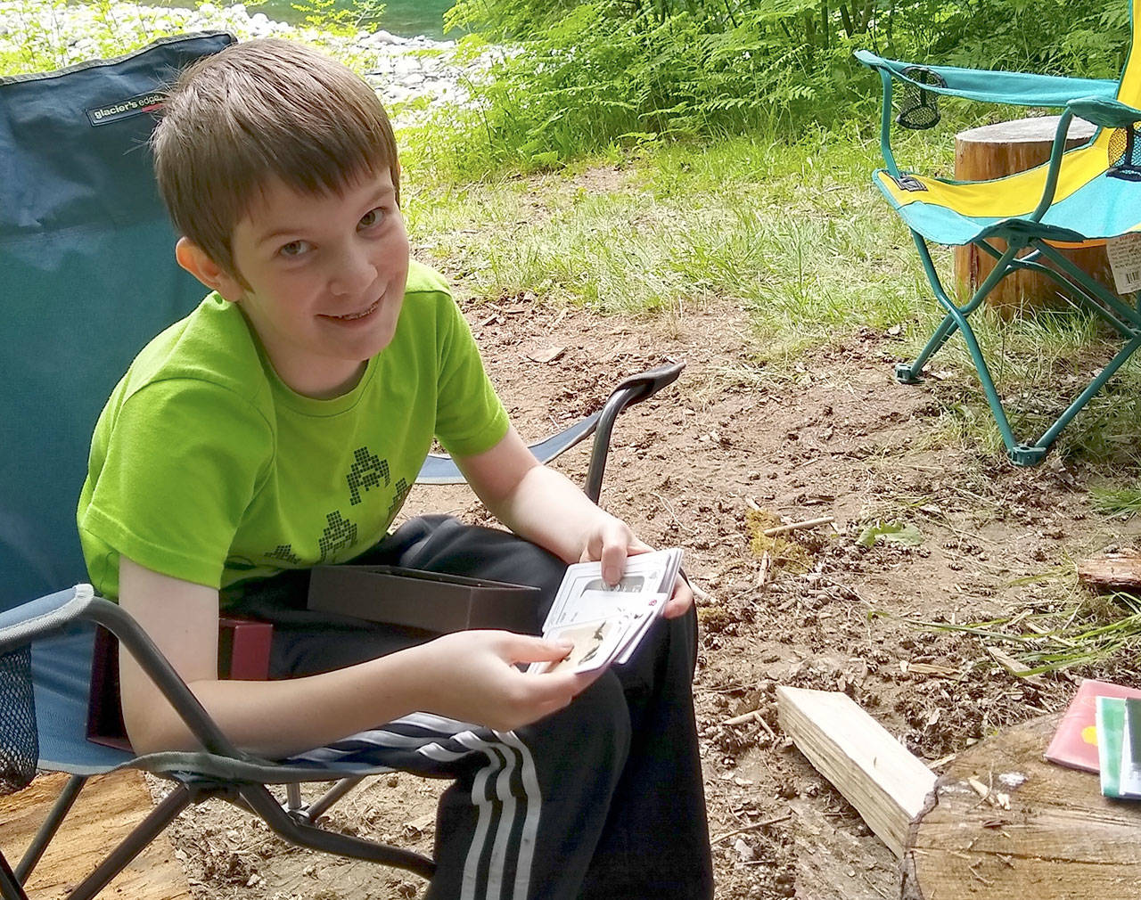 Luke, 11, tries to explain the card game Exploding Kittens while out camping with his family on their Sol Duc River property. (Zorina Barker/for Peninsula Daily News)