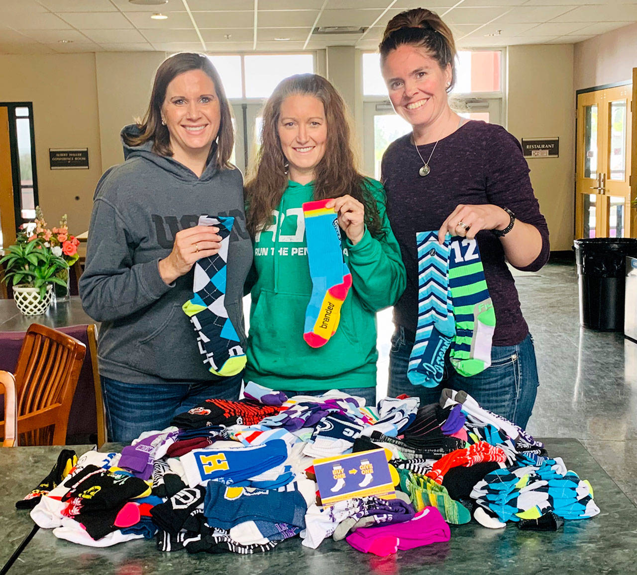 Port Angeles Marathon Association race Director Victoria Jones, center, with Caring for Kids co-founders, Jessica Johnson, right, and Jennifer Riffle, left. The marathon association donated more than $1,000 in socks to Caring for Kids.