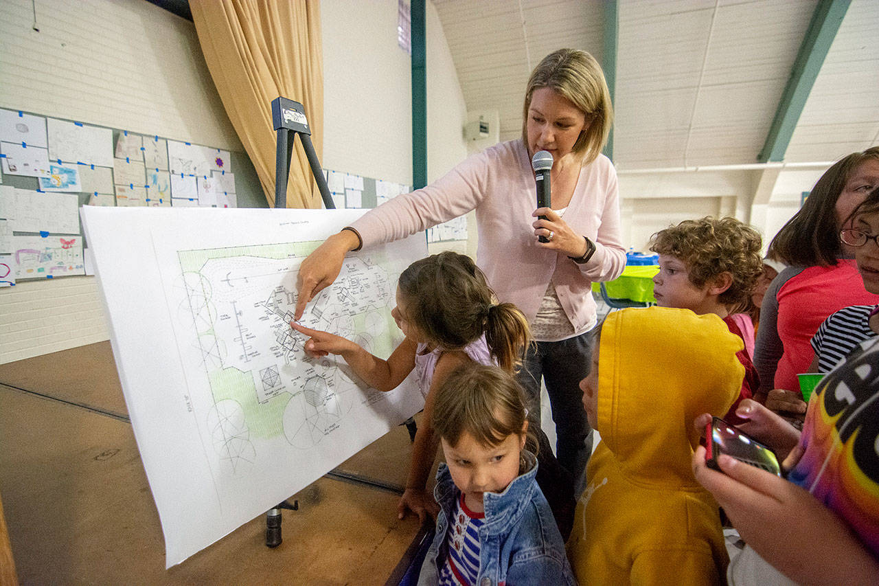 Children crowd around as Laura Sehn, project manager with Play By Design, unveils a conceptual drawing of the “Generation II” Dream Playground. The new playground will feature a treehouse, a castle and a zipline. (Jesse Major/Peninsula Daily News)