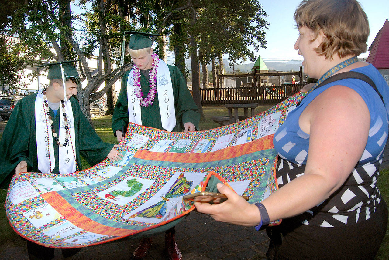 Louisa Monger, a teacher at Dry Creek School and formerly at Jefferson School, right, shows off a quilt made 10 years ago from squares created by her students, including Port Angeles High School seniors Charles Krause, left, and Tristian Turner, prior to commencement ceremonies on Friday evening at Port Angeles Civic Field. More than 230 students were scheduled to become part of the Class of 2019. (Keith Thorpe/Peninsula Daily News)