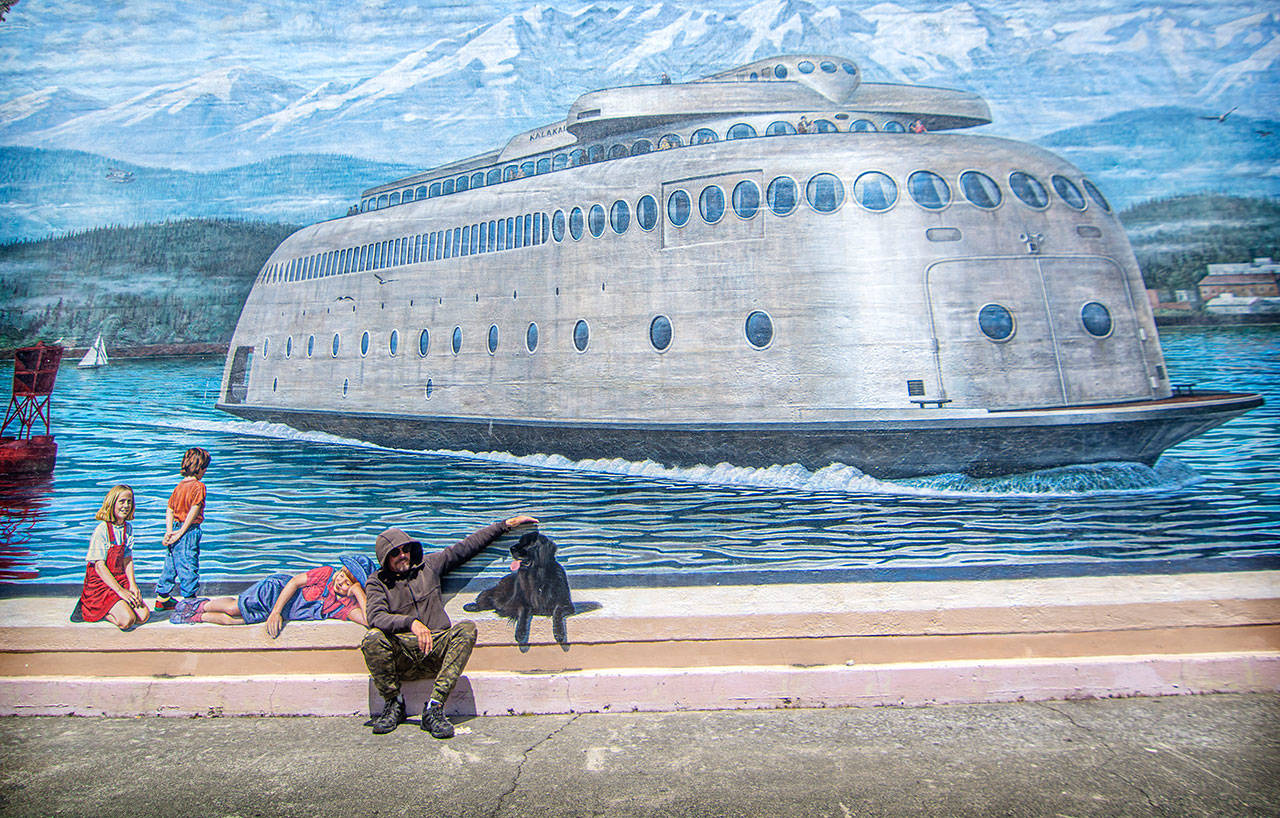 Cory Ench sits in front of the MV Kalakala mural in downtown Port Angeles. Ench is restoring three 1990s murals this summer — the Kalakala, Sluicing the Hogback and I’e’nis/Ennis Creek — as part of a $45,600 Nor’wester Rotary Club of Port Angeles project. (Jesse Major/Peninsula Daily News)
