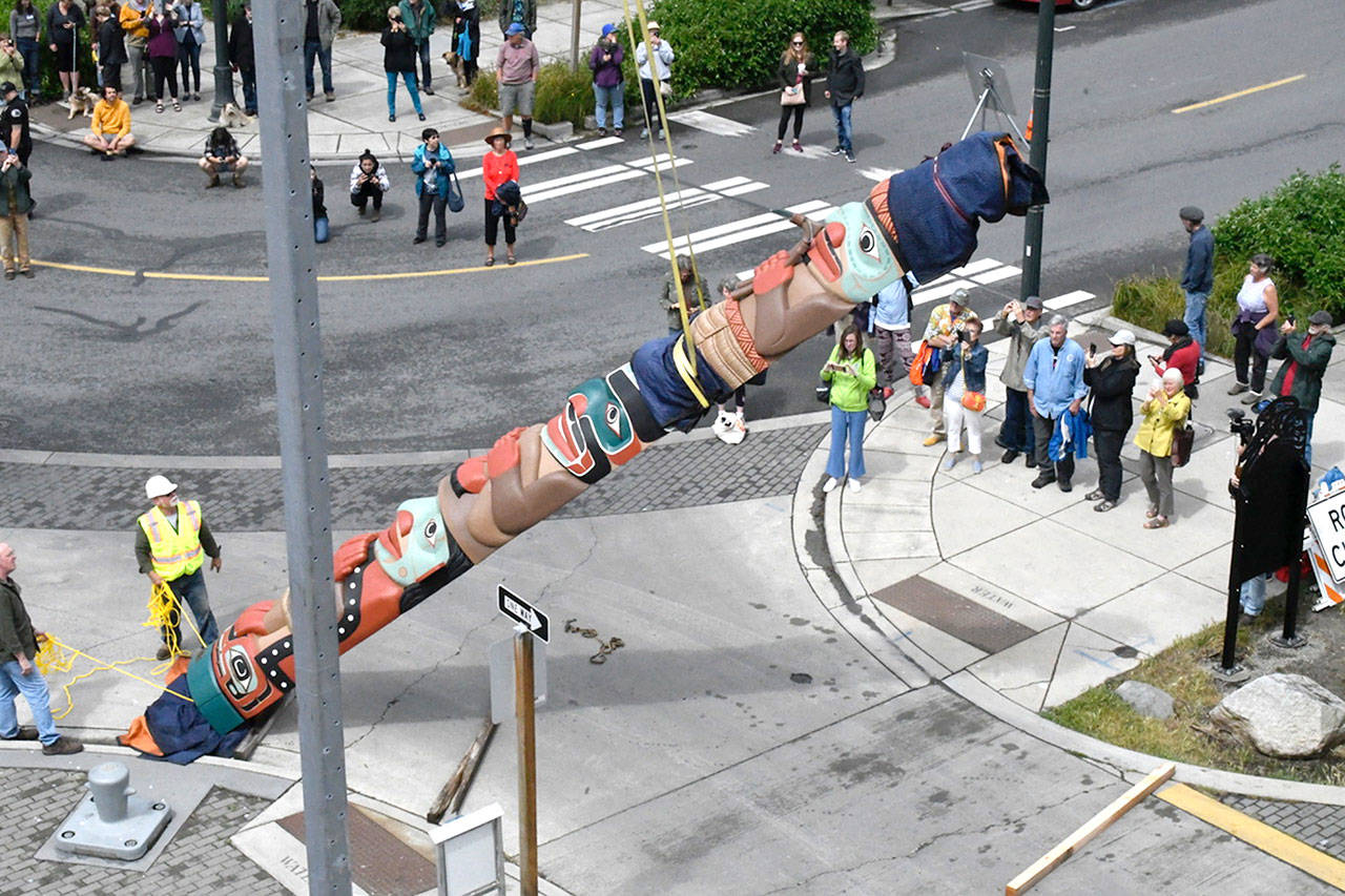 A 26-foot Jamestown S’Klallam Tribe totem pole was placed in front of the Northwest Maritime Center on Thursday. Created by master carver Dale Faulstich, the 1,600-pound art piece joins a carved canoe and signage at the Wooden Boat Chandlery. The job took about 90 minutes and over 100 people witnessed the work done by a crane operator and installation team. (Jeannie McMacken/Peninsula Daily News)