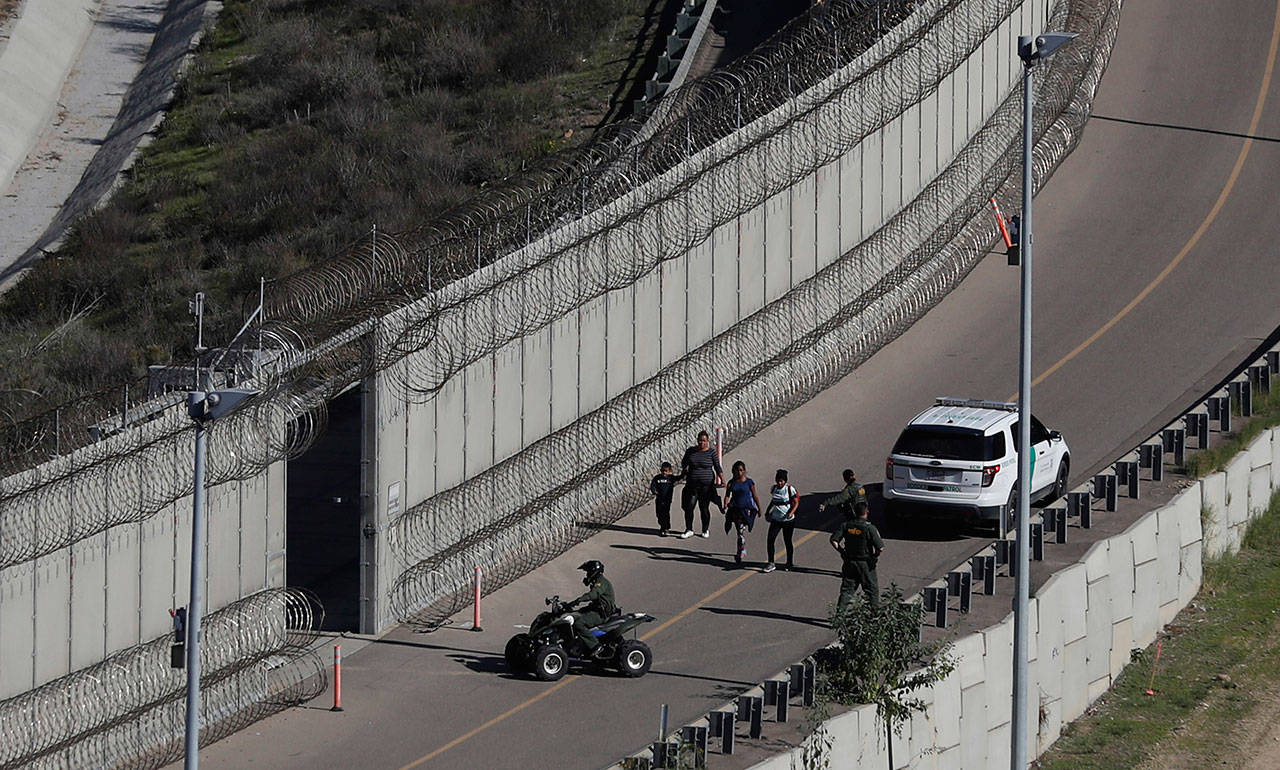 In this Dec. 16, 2018, file photo, Honduran asylum seekers are taken into custody by U.S. Border Patrol agents after the group crossed the U.S. border wall into San Diego in this view from Tijuana, Mexico. (Moises Castillo/The Associated Press)