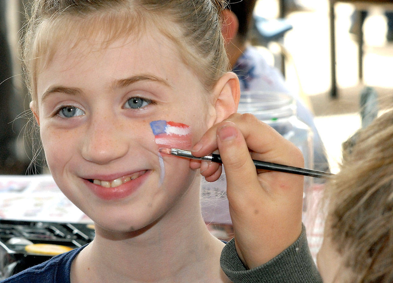 Makenzy Thompson of Port Angeles receives an American flag from face painter Abby Sanford in honor of Independence Day at the children’s activity area in the pavilion at The Gateway transit center in Port Angeles in 2018. (Keith Thorpe/Peninsula Daily News)