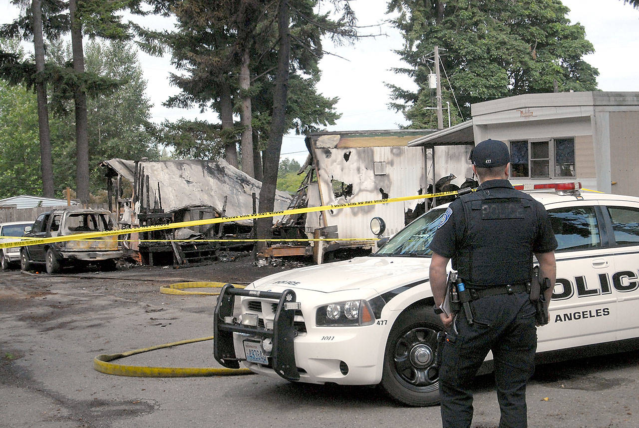 Port Angeles police officer T.J. Mueller looks over the scene of a fire that left four dead and destroyed two mobile homes early Saturday at the Welcome Inn RV Park in Port Angeles. (Keith Thorpe/Peninsula Daily News)