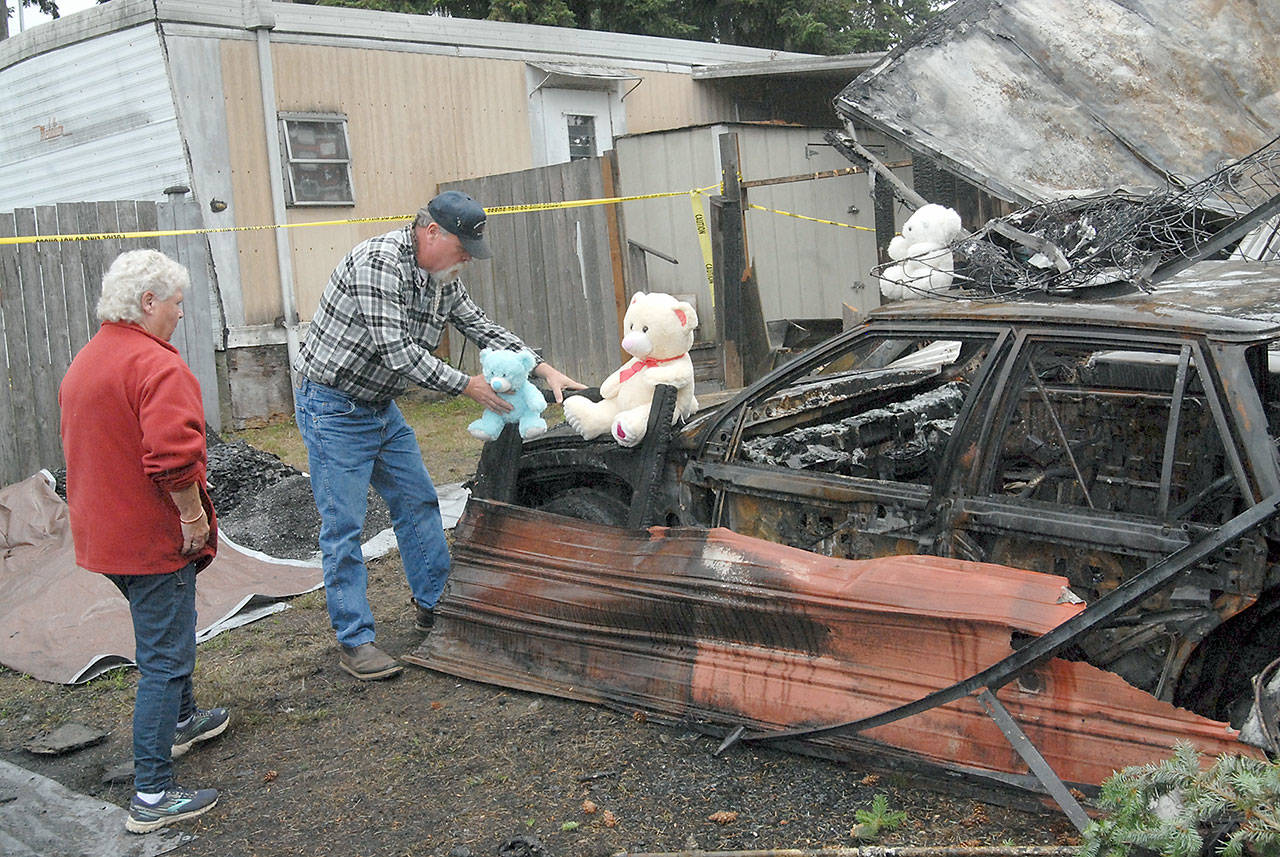 Jack Hutto of Port Angeles, grandfather to children Lilly Kambeitz, Emma Kambeitz and Jayden Kambeitz, accompanied by his mother, Pat Hutto, on Wednesday places teddy bears that belonged to his grandchildren next to the burned mobile home where the Kambeitz family was discovered after the house burned Saturday morning at the Welcome Inn RV Park in Port Angeles. (Keith Thorpe/Peninsula Daily News)
