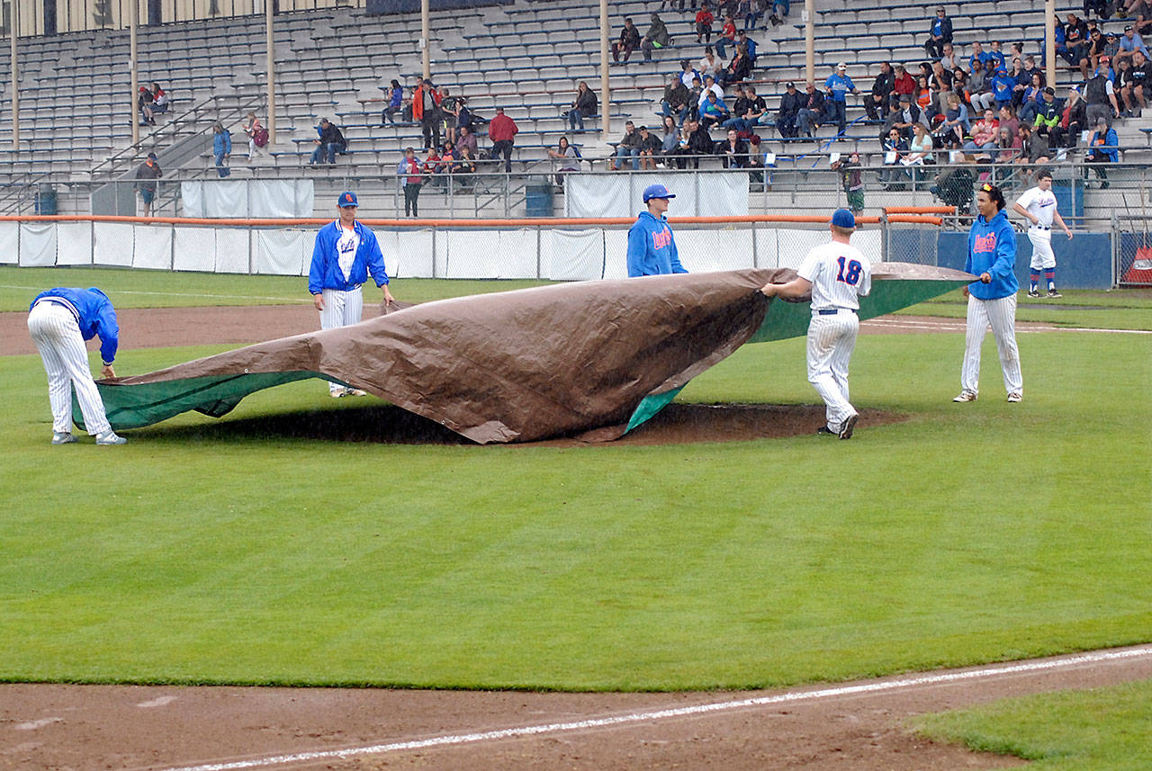 Lefties players spread a tarp over the pitcher’s mound as heavy rain pours down on Port Angeles Civic Field on Wednesday evening. The rainstorm drenched the stadium, and coaches and game officials declared the field unplayable, forcing cancellation of the Lefties game against the Corvallis Knights in the top of the second inning with no score.                                Keith Thorpe/Peninsula Daily News