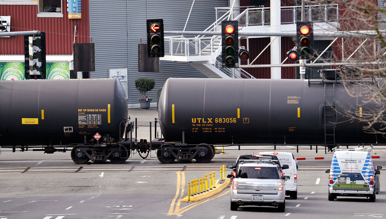 In this 2018 photo, automobile traffic waits at a train crossing as train cars that carry oil are pulled through downtown Seattle. (Elaine Thompson/The Associated Press)