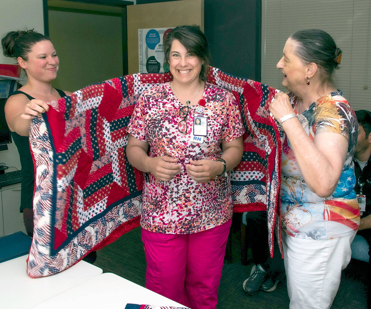 Renee Tyler, left, assists JoEllen Thompson of Jefferson County Quilts of Valor, on right, with the presentation of a quilt to former U.S. Navy mineman Tracy Delacruz. Delacruz is an RN at the VA clinic in Port Angeles.