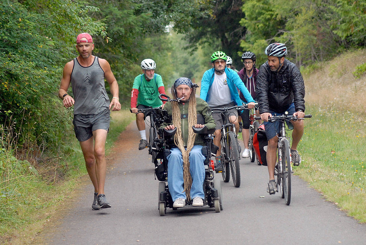 Ian Mackay of Agnew, center, leads a contingent of friends and supporters on bicycles and on foot from his motorized wheelchair along the Olympic Discovery Trail near 18th Street in Port Angeles during Saturdays segment of the three-day Sea to Sound group ride across a portion of the North Olympic Peninsula. (Keith Thorpe/Peninsula Daily News)