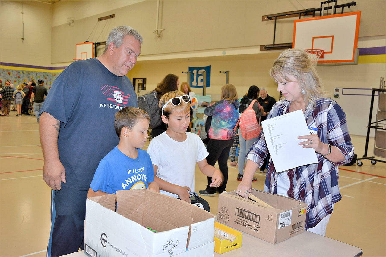 From left, Jason Bondy with his sons, Roosevelt Elementary second-grader Xyler Brown and fourth-grader Tryton Bondy, goes through the school supply line assisted by volunteer navigator Terri Brewer. (Patsene Dashiell/Port Angeles School District)