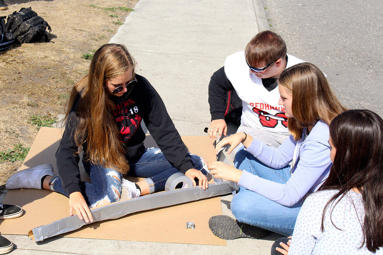Port Townsend High School sophomore Savannah Hoffman, left, works with her classmates to build a boat out of cardboard and duct tape. Their boat was christened “Quack Attack” and competed against other boats built by their classmates later in the day. (Zach Jablonski/Peninsula Daily News)
