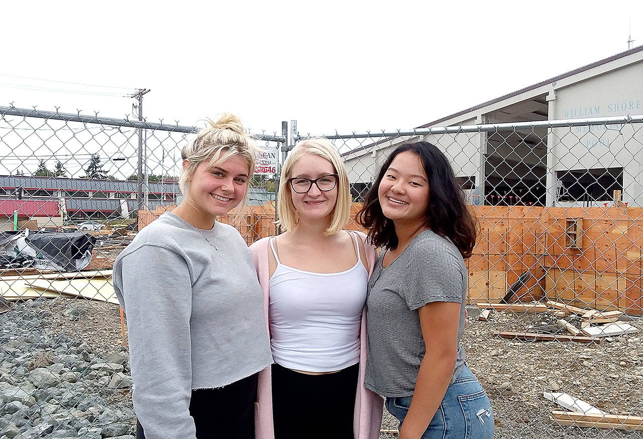 Port Angeles seniors, from left, Kenzie Johnson, Emma Murray and Felicia Che lead a team that has no home pool this season. Behind them, workers are busy rebuilding the William Shore Memorial Pool. (Pierre LaBossiere/Peninsula Daily News)