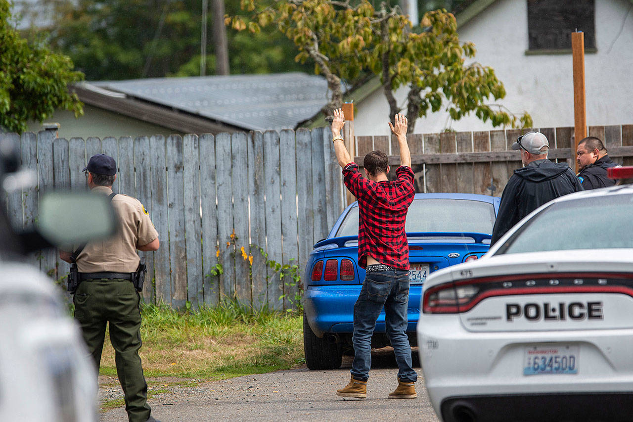 Alex Frost, who was charged Monday with possession of a stolen vehicle and second-degree possession of stolen property, holds his hands over his head before being handcuffed at the Welcome Inn RV Park on Thursday. (Jesse Major/Peninsula Daily News)