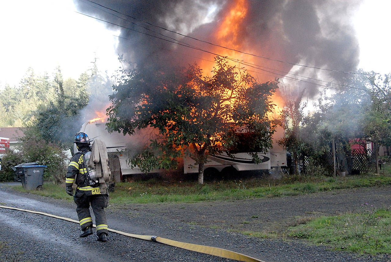 Port Angeles firefighter Tyler Gage carries a hose to the scene of a blaze that destroyed a travel trailer on West 15th Street on Thursday morning. (Keith Thorpe/Peninsula Daily News)