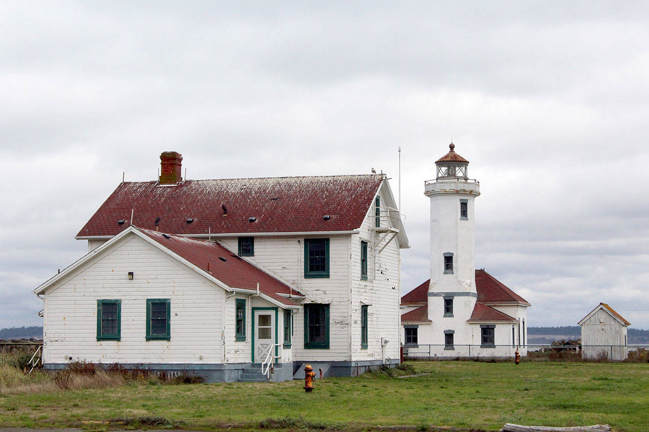 Point Wilson Lighthouse can be seen behind one of the original dwellings and original home of the light. Point Wilson has now been leased to the U.S. Lighthouse Society for restoration. (Zach Jablonski/Peninsula Daily News)