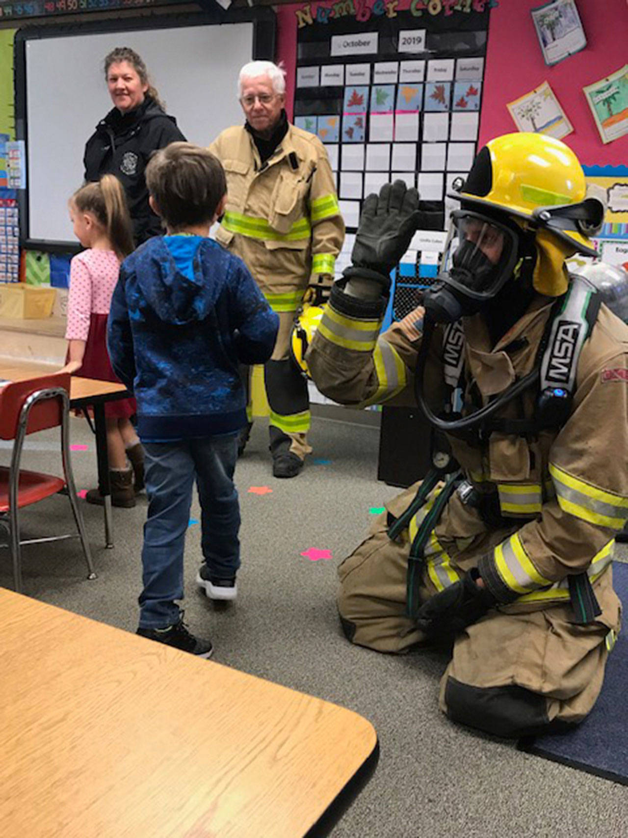 Clallam Fire District No. 4 EMTs Suzie Frantz and Lee Evinger watch as students high five firefighter Matthew Shreeve. (Clallam Fire District No. 4)