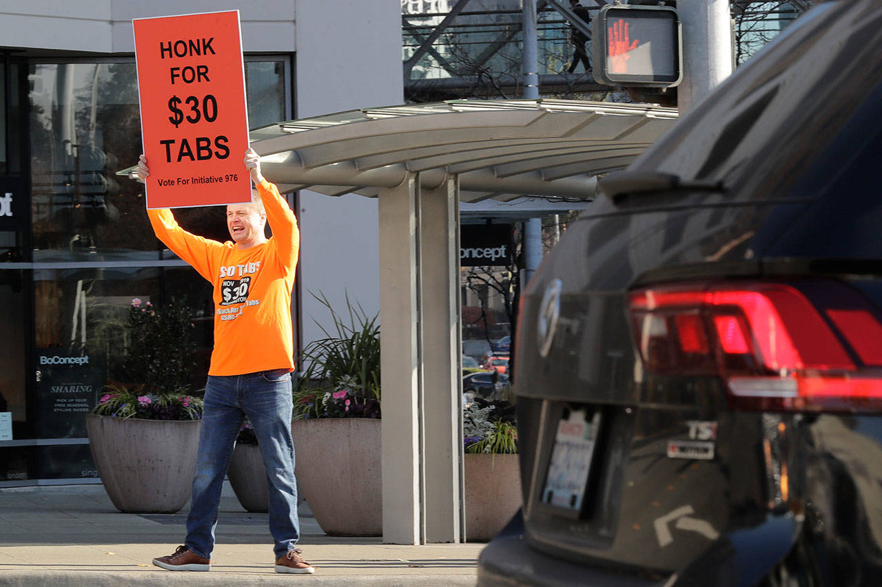 Anti-tax activist Tim Eyman holds a sign supporting Initiative 976, which would cut most car registration tabs to $30 in Washington state, Tuesday on election day in Bellevue. (Ted S. Warren/The Associated Press)