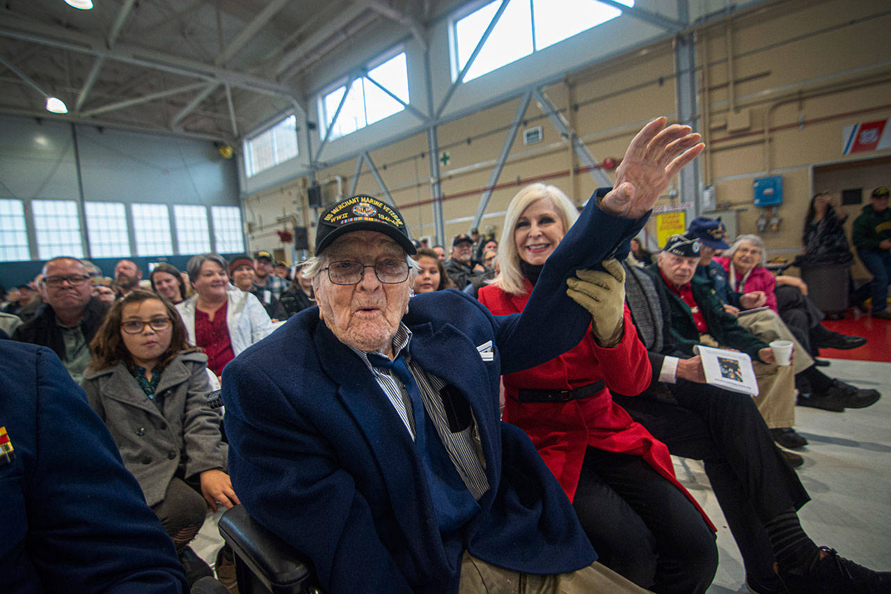Port Angeles City Councilmember Cherie Kidd helps World War II veteran William Payne, of the Merchant Marine, raise his hand as Rear Adm. Christopher Gray of the U.S. Navy searches for the oldest veteran at the Veterans Day ceremony at U.S. Coast Guard Air Station/Sector Field Office Port Angeles on Monday. (Jesse Major/Peninsula Daily News)