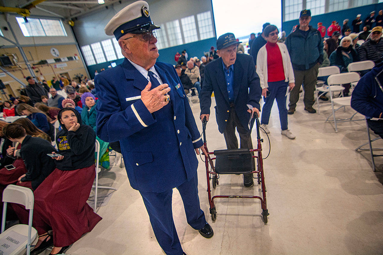 Richard Fleck of the Coast Guard Auxillary finds a seat for Navy veteran Frank Meek, who served during World War II, during the Veterans Day ceremony at U.S. Coast Guard Air Station/Sector Field Office Port Angeles on Monday. (Jesse Major/Peninsula Daily News)