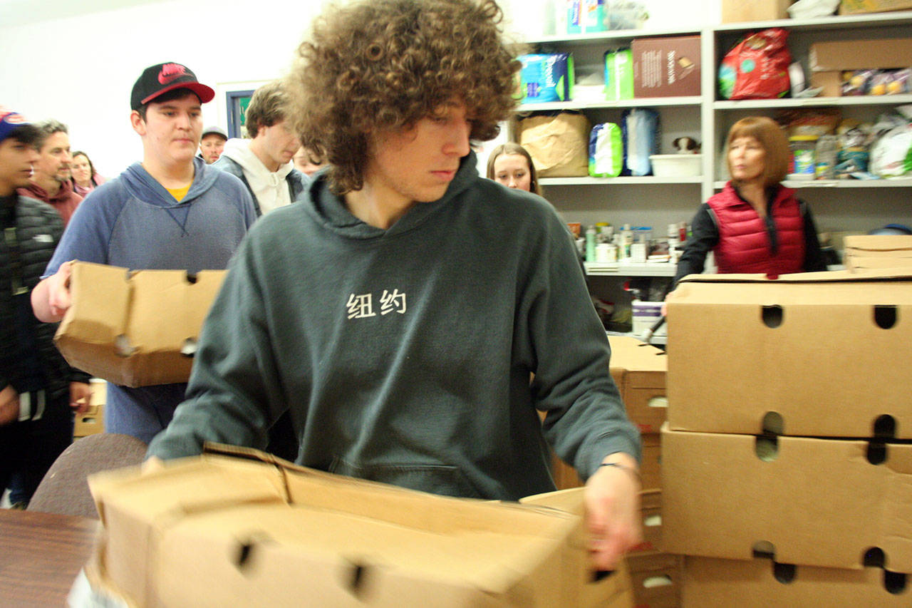 Port Townsend High School student Aidan Falge carries a box with four turkeys donated by Arrow Lumber to a staging area inside the Port Townsend Food Bank on Monday. Additional volunteers, including Payton Berg, left, helped to carry 375 donated turkeys. (Brian McLean/Peninsula Daily News)
