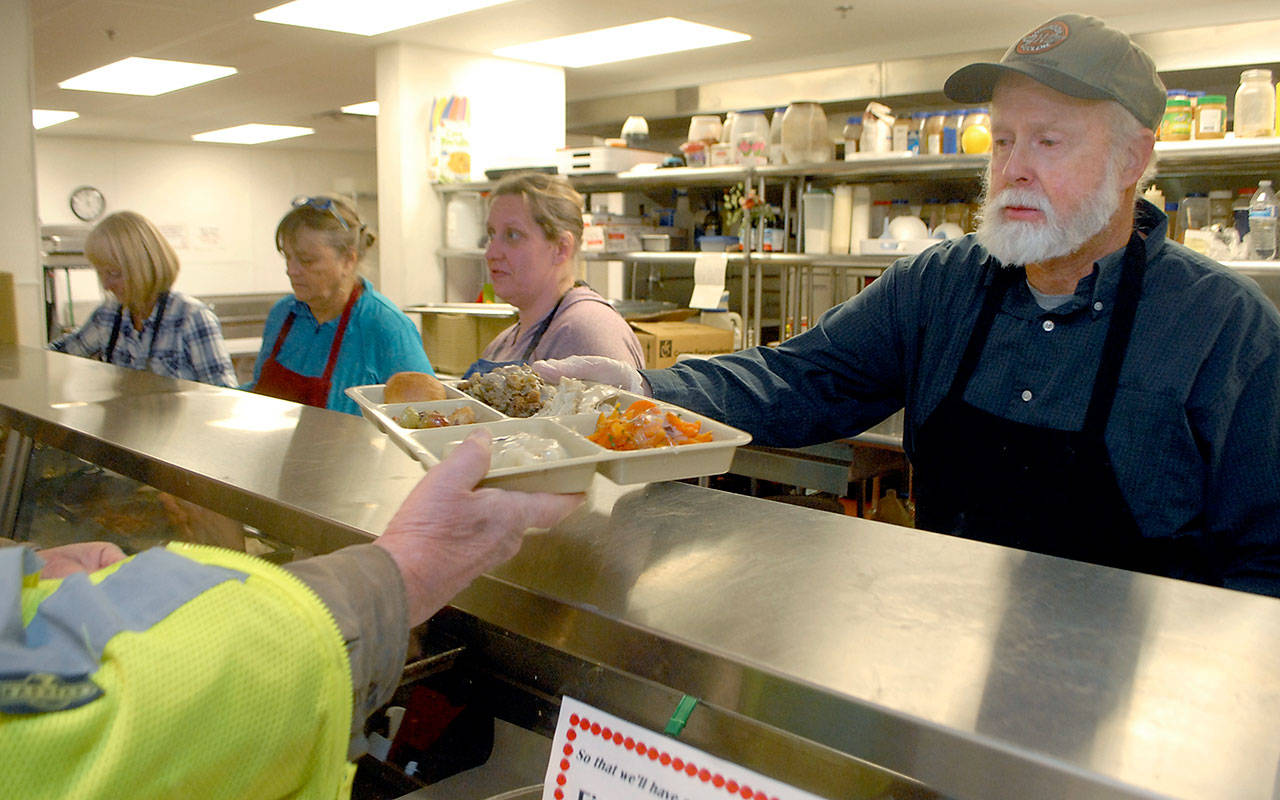 Doug Crabb of Sequim, right, hands out a dinner tray as volunteers, from left, Phyllis Meyer of Sequim, Linda Crabb of Sequim and Darci McCabe of Port Angeles prepare meals for Wednesday’s Thanksgiving Eve lunch at the Port Angeles Salvation Army kitchen. (Keith Thorpe/Peninsula Daily News)