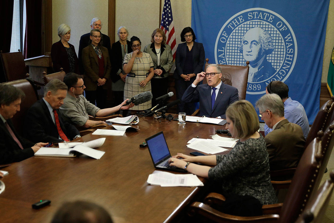 Gov. Jay Inslee, seated center, talks to reporters about his proposed supplemental state budget on Wednesday at the Capitol in Olympia. (Ted S. Warren/The Associated Press)