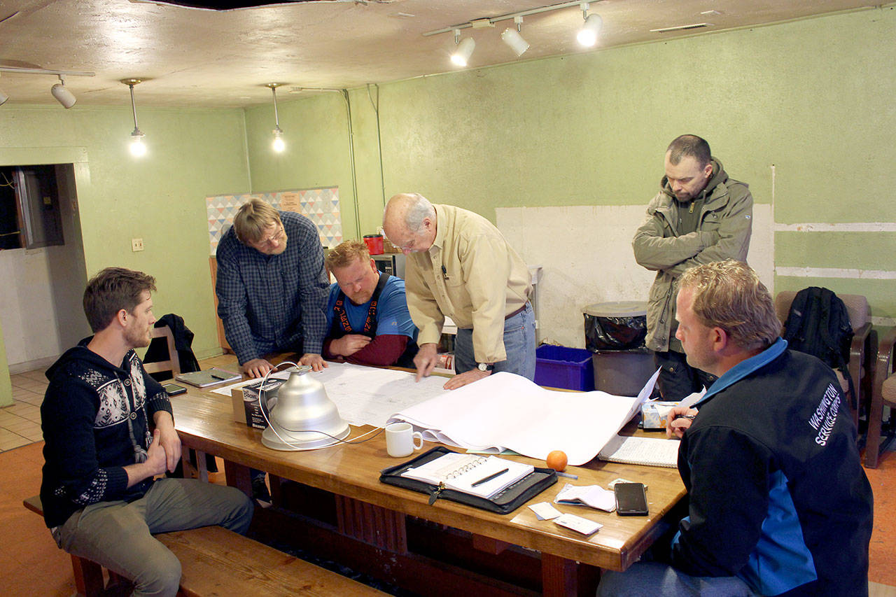 Jim Rozanski, in yellow, lead architect for the Recovery Cafe and owner of Rozanski Architects, leads the discussion of the renovation plans with other foreman of the Dove House Recovery Cafe at the cafe. The team along with volunteers will begin the structural renovations to the cafe on Monday. (Zach Jablonski/Peninsula Daily News)