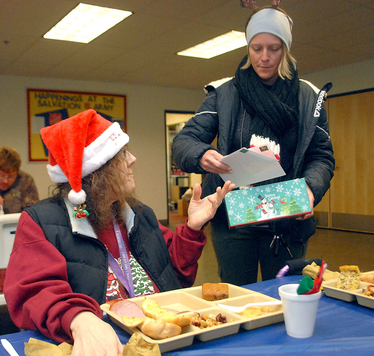 Amy Miller of the Rediscovery program, standing, passes out pre-stamped Christmas cards to Kathryn Brown of Port Angeles during Tuesday’s Christmas Eve lunch at the Salvation Army kitchen in Port Angeles. (Keith Thorpe/Peninsula Daily News)